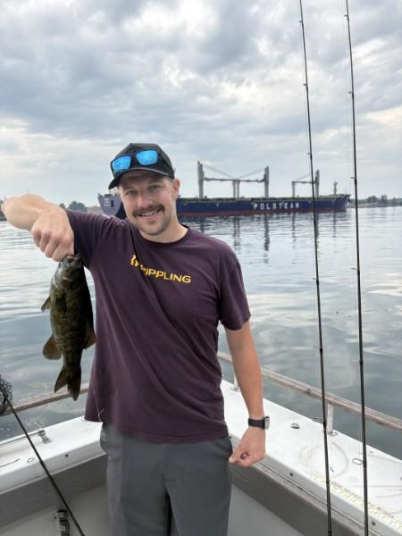 Angler holding up his catch with a freighter passing in the shipping channel