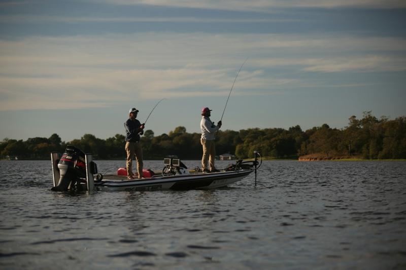 Two anglers casting from a bass boat at dusk