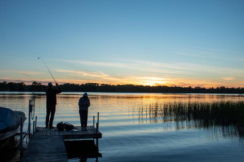 Two anglers fishing from a dock as the sun goes down