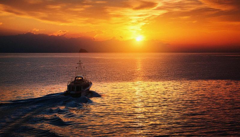 A boat heading home across the water at sunset