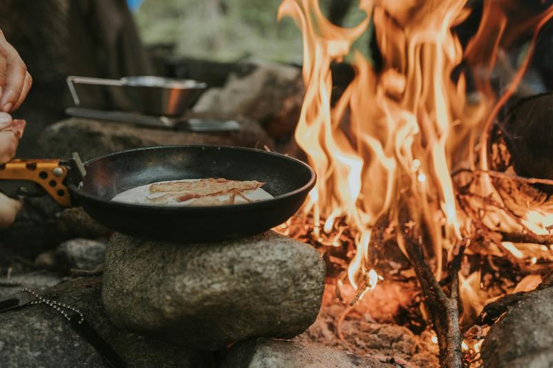 A skillet of food cooking beside an open fire on the rocks