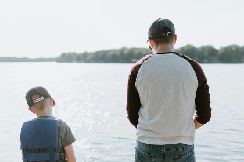 A father and son fishing side by side from the shore