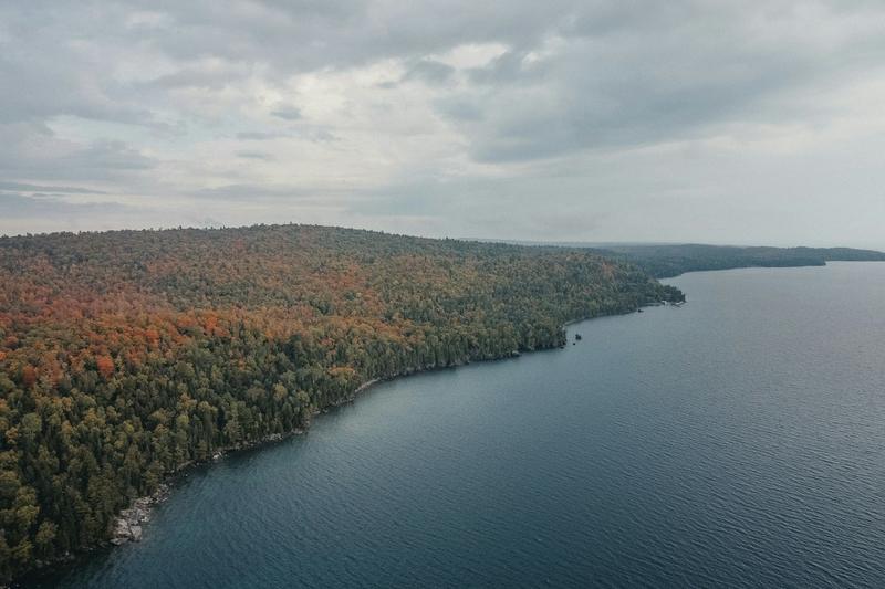 Fall color along a long wooded shoreline above calm water