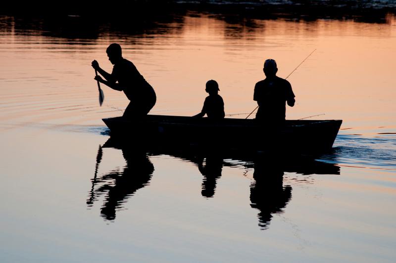 Silhouette of three people fishing from a small boat at sunset