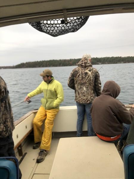 Three anglers in rain gear fishing from the boat on a cool, gray day