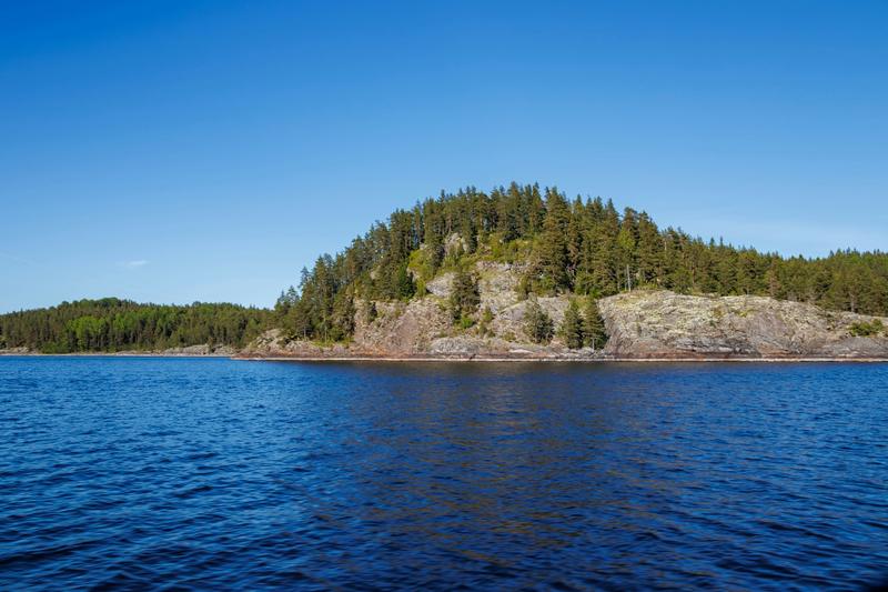 A wooded island with a rocky base in calm blue water