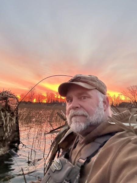 Hunter in camo in a duck blind at a fiery orange sunrise