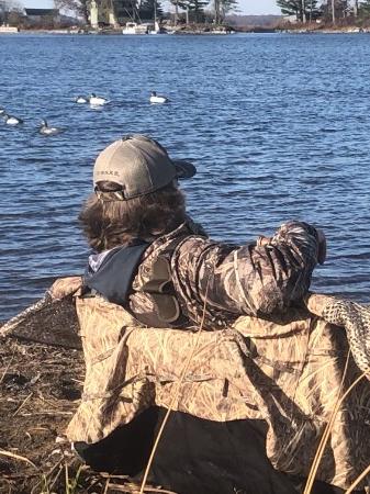 Hunter in a layout blind on the shoreline with decoys on the water