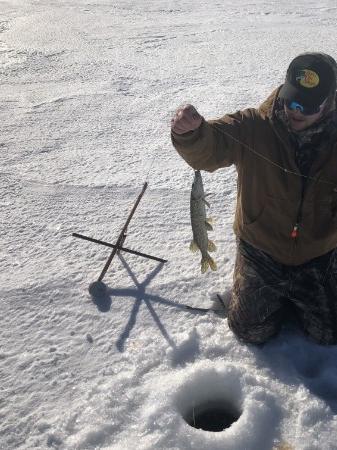 Kneeling angler holding a pike beside an ice hole and tip-up