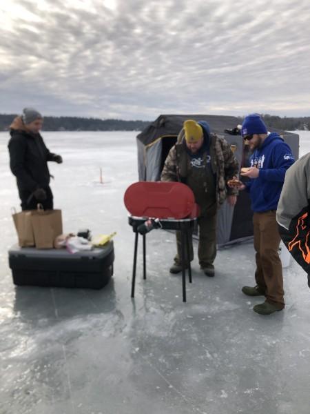 Anglers gathered around a grill and a shanty on the frozen river