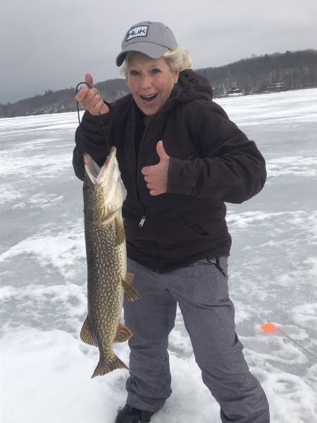 Angler giving a thumbs up while holding a long northern pike on the ice