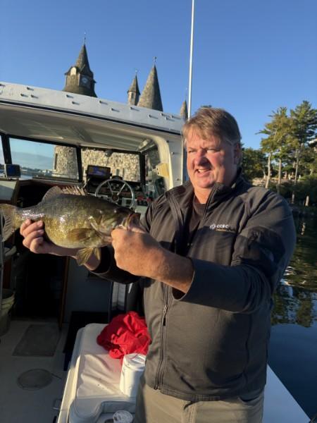 Angler on Richard's boat holding a large smallmouth bass, with castle turrets in the background