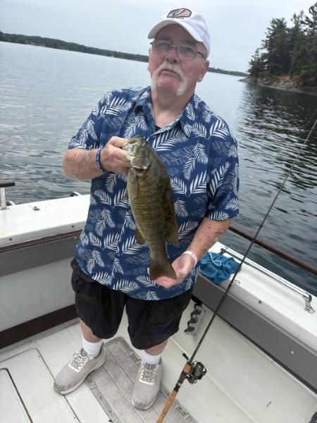 Smiling angler in a Hawaiian shirt holding a smallmouth bass on the boat