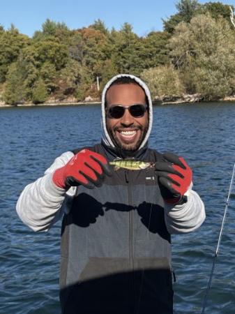 Grinning angler in red gloves holding up a fish in front of a wooded island