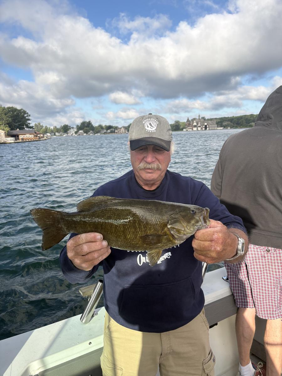 Richard Drake holding a big St. Lawrence River smallmouth bass, with the Boldt Yacht House behind him