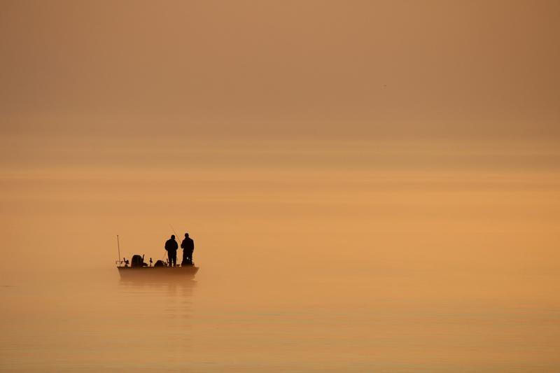 Two anglers fishing from a small boat at sunrise