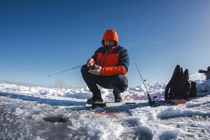 An angler in an orange jacket jigging through a hole in the ice