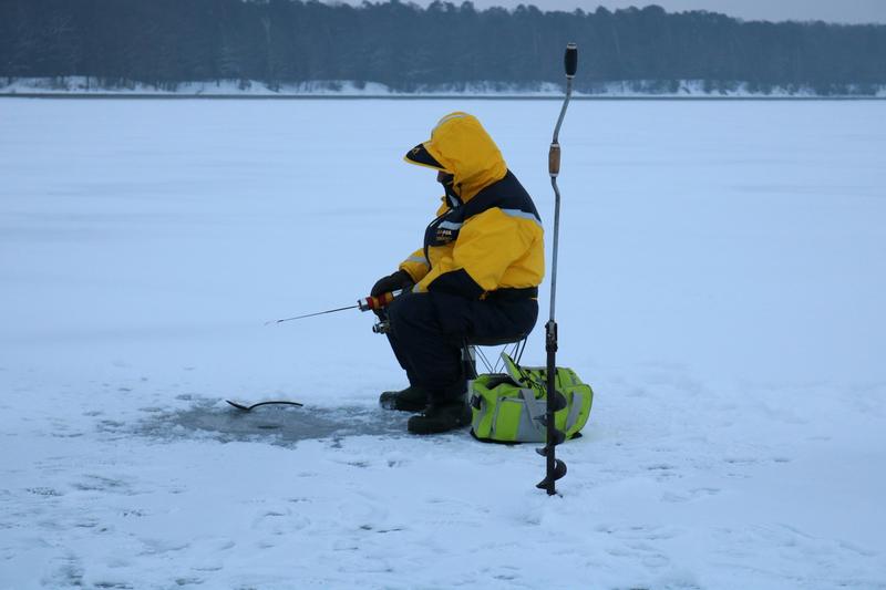 An angler ice fishing beside an auger on a frozen lake