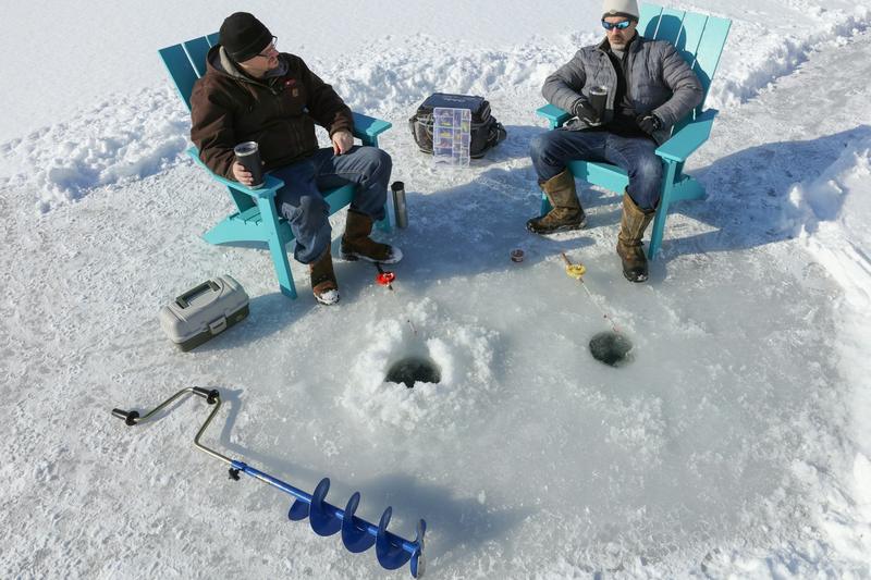 Two anglers in chairs fishing through holes in the ice, with an auger beside them