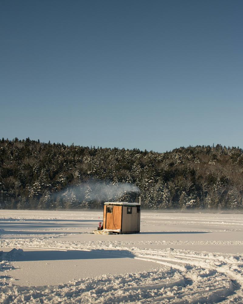 An ice fishing shanty on a frozen lake with smoke rising from the chimney